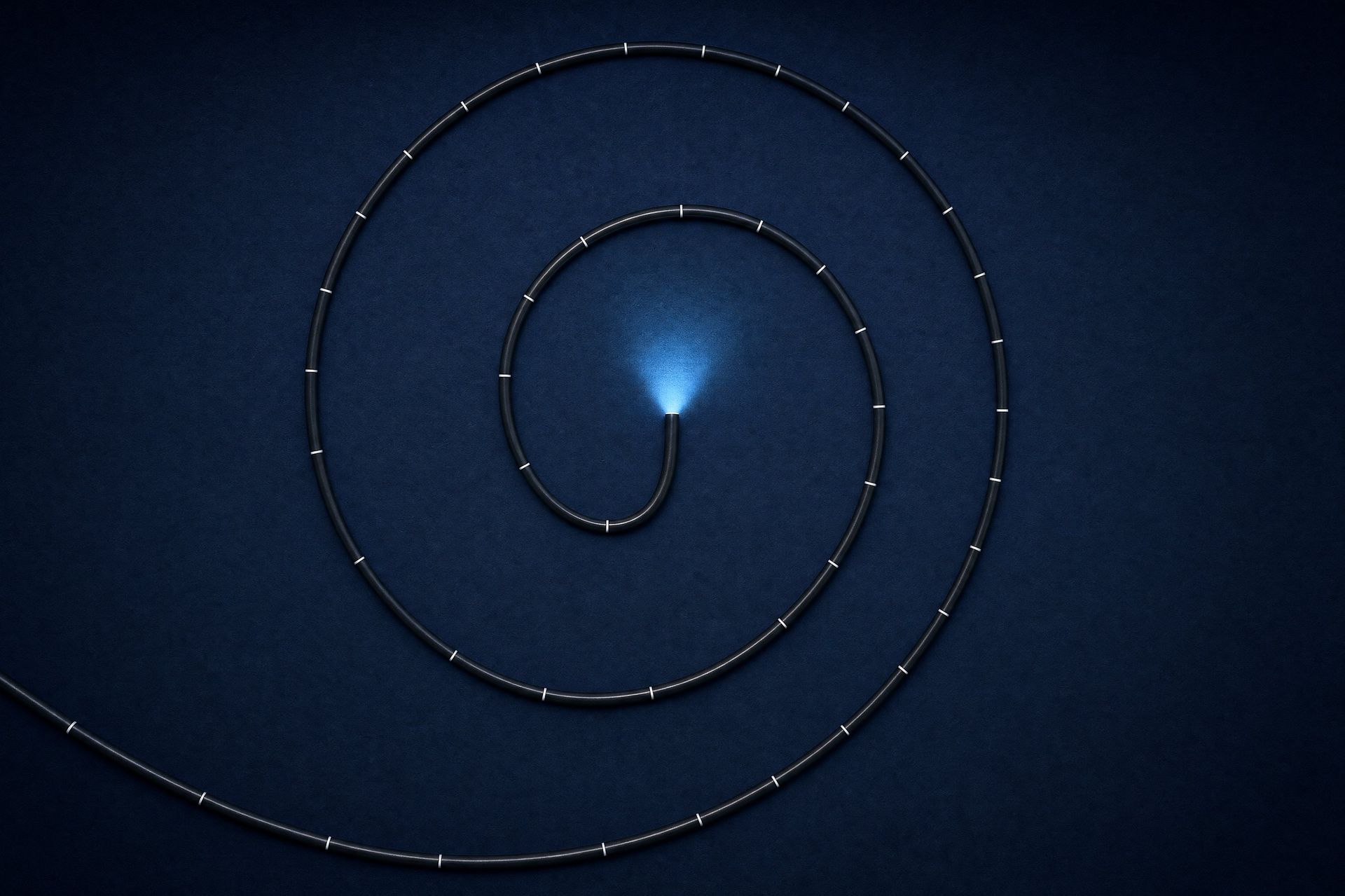 Tubo de um endoscópio enrolado em espiral sobre fundo azul-marinho, com a luz da ponta acesa no centro
